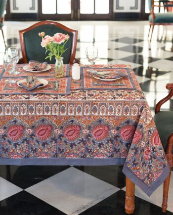 Une table joliment dressée comprenant la nappe Delhi Floral, des sets de table assortis, des serviettes, de la verrerie, de l'argenterie et un vase de roses roses, créant une ambiance élégante et accueillante.