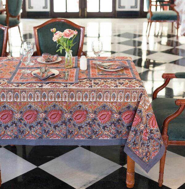 Une table joliment dressée comprenant la nappe Delhi Floral, des sets de table assortis, des serviettes, de la verrerie, de l'argenterie et un vase de roses roses, créant une ambiance élégante et accueillante.