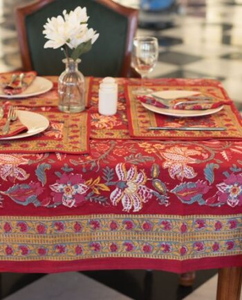 "Nappe rouge Maharani Glow avec des motifs floraux indiens complexes en jaune, rose et vert. Évoque une ambiance chaleureuse et luxueuse