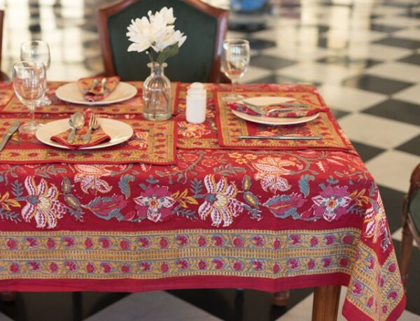 "Nappe rouge Maharani Glow avec des motifs floraux indiens complexes en jaune, rose et vert. Évoque une ambiance chaleureuse et luxueuse