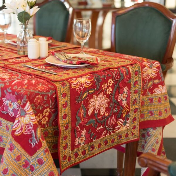 Nappe rouge Maharani Glow avec des motifs floraux indiens complexes en jaune, rose et vert. Évoque une ambiance chaleureuse et luxueuse