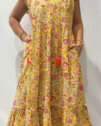 Robe Chandra Jaune - Femme portant une robe longue sans manches à imprimé floral, avec volants et liens à pompons, coupe ample et col tunisien.