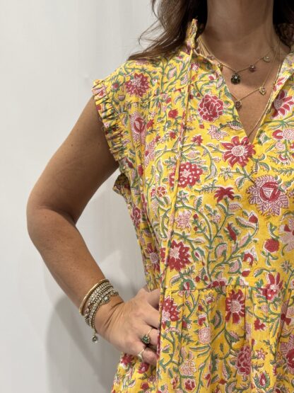 Robe Chandra Jaune - Femme portant une robe longue sans manches à imprimé floral, avec volants et liens à pompons, coupe ample et col tunisien.