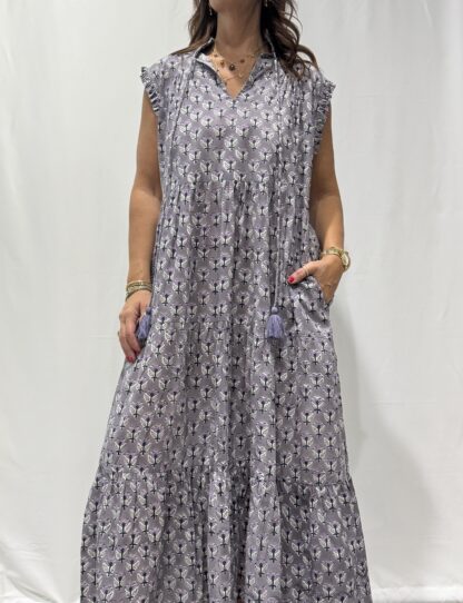 Robe Chandra Mauve Fleurie - Femme portant une robe longue sans manches à imprimé floral, avec volants et liens à pompons, coupe ample et col tunisien.