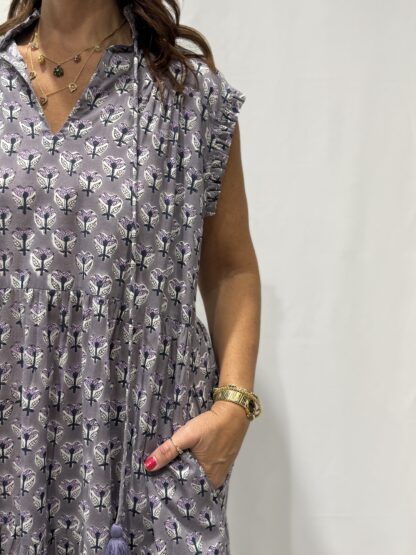 Robe Chandra Mauve Fleurie - Femme portant une robe longue sans manches à imprimé floral, avec volants et liens à pompons, coupe ample et col tunisien.