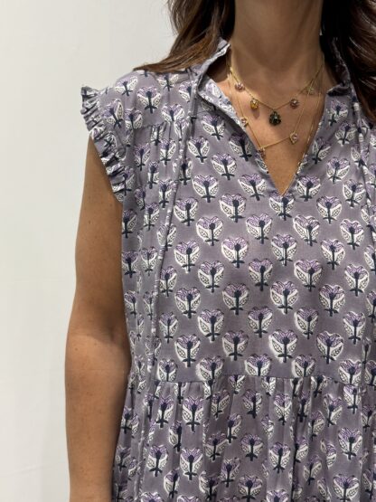 Robe Chandra Mauve Fleurie - Femme portant une robe longue sans manches à imprimé floral, avec volants et liens à pompons, coupe ample et col tunisien.