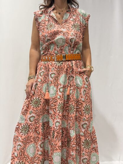 Robe Chandra Rose - Femme portant une robe longue sans manches à imprimé floral, avec volants et liens à pompons, coupe ample et col tunisien.