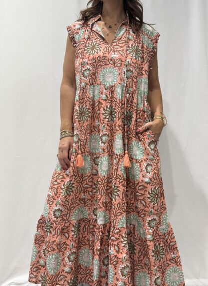 Robe Chandra Rose - Femme portant une robe longue sans manches à imprimé floral, avec volants et liens à pompons, coupe ample et col tunisien.