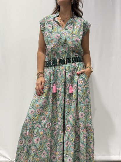 Robe Chandra Verte Fleurie - Femme portant une robe longue sans manches à imprimé floral, avec volants et liens à pompons, coupe ample et col tunisien.