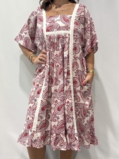 Robe Mallika blanche framboise : Femme portant une robe blanche à imprimé floral rouge framboise et mauve avec empiècements contrastés blanc et manches courtes amples.