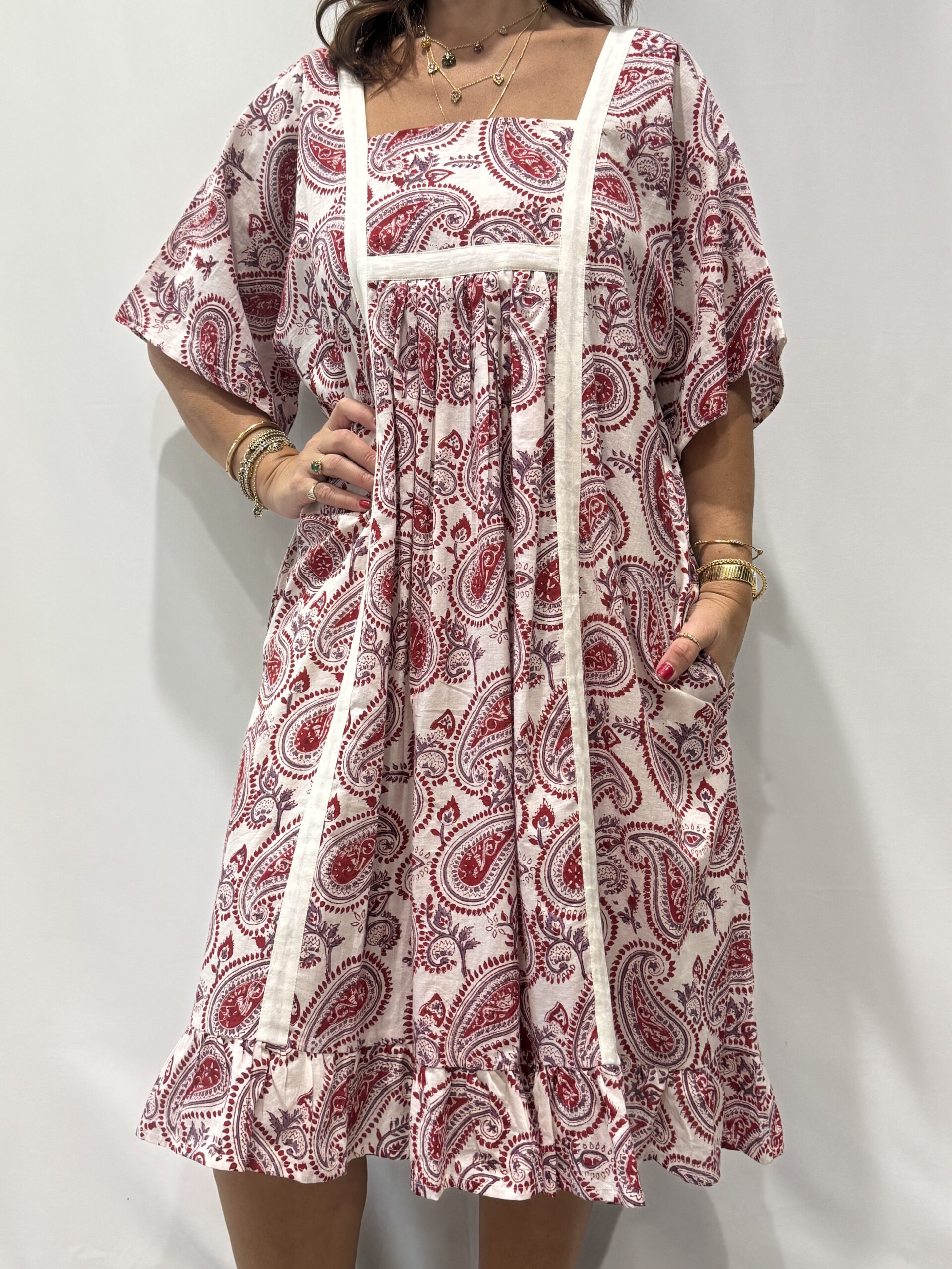 Robe Mallika blanche framboise : Femme portant une robe blanche à imprimé floral rouge framboise et mauve avec empiècements contrastés blanc et manches courtes amples.