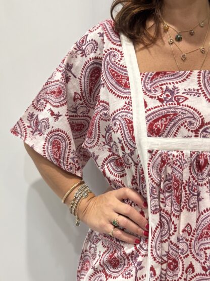 Robe Mallika blanche framboise : Femme portant une robe blanche à imprimé floral rouge framboise et mauve avec empiècements contrastés blanc et manches courtes amples.