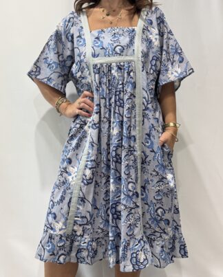 Robe Mallika Bleu : Femme portant une robe bleu à imprimé floral bleu gris et blanc avec empiècements contrastés bleu et manches courtes amples.