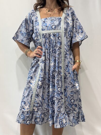 Robe Mallika Bleu : Femme portant une robe bleu à imprimé floral bleu gris et blanc avec empiècements contrastés bleu et manches courtes amples.