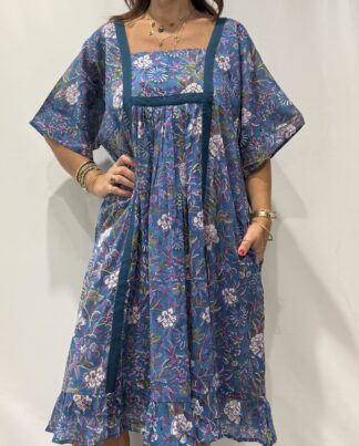 Robe Mallika bleu mauve : Femme portant une robe bleu à imprimé floral vert et violet avec empiècements contrastés bleu et manches courtes amples.