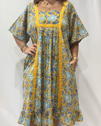 Robe Mallika Jaune Bleu : Femme portant une robe jaune à imprimé floral bleu avec empiècements contrastés jaune et manches courtes amples.