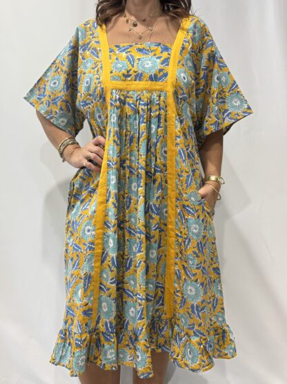 Robe Mallika Jaune Bleu : Femme portant une robe jaune à imprimé floral bleu avec empiècements contrastés jaune et manches courtes amples.