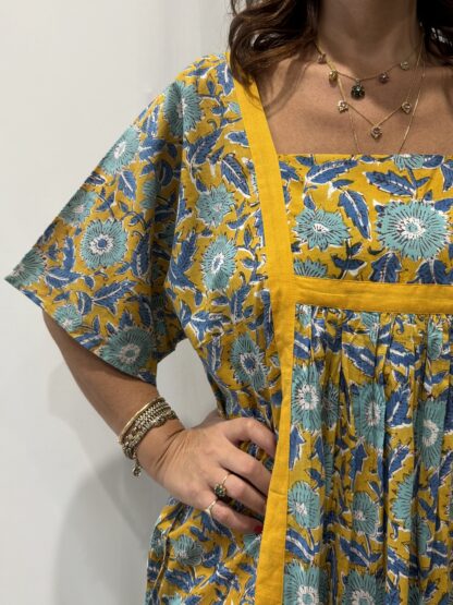 Robe Mallika Jaune Bleu : Femme portant une robe jaune à imprimé floral bleu avec empiècements contrastés jaune et manches courtes amples.
