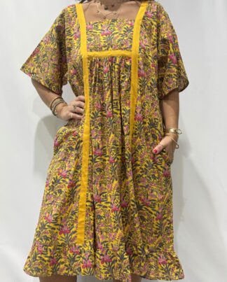 Robe Mallika Jaune Fleurie : Femme portant une robe jaune à imprimé floral vert et rose avec empiècements contrastés jaunes et manches courtes amples.