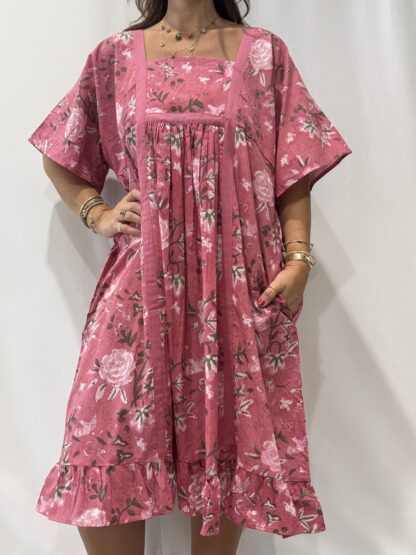 Robe Mallika Rose : Femme portant une robe à imprimé floral rose et vert, avec empiècements contrastés jaunes et manches courtes amples.