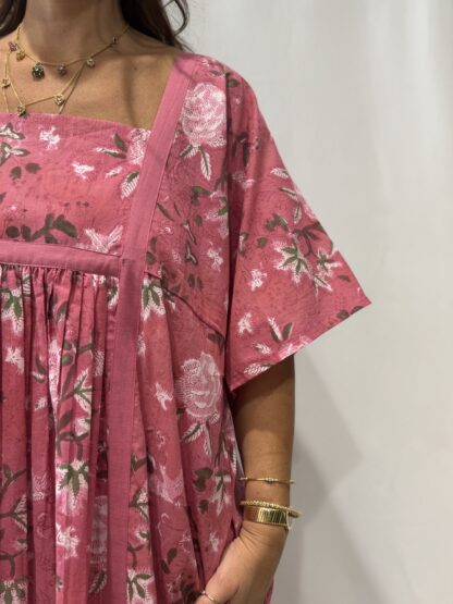 Robe Mallika Rose : Femme portant une robe à imprimé floral rose et vert, avec empiècements contrastés jaunes et manches courtes amples.