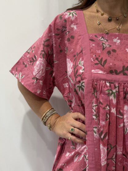 Robe Mallika Rose : Femme portant une robe à imprimé floral rose et vert, avec empiècements contrastés jaunes et manches courtes amples.