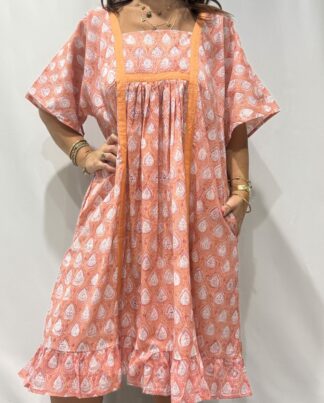Robe Mallika Saumon : Femme portant une robe rose saumon à imprimé floral blanc avec empiècements contrastés rose saumon et manches courtes amples.