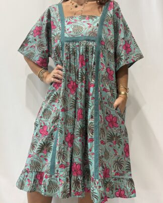 Robe Mallika Verte Rose : Femme portant une robe verte à imprimé floral rose et vert, avec empiècements contrastés jaunes et manches courtes amples.