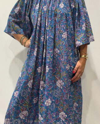 Robe Sita Bleu Mauve -Femme portant une robe ample en coton bleu et mauve à imprimé floral, manches larges et col smocké en dentelle