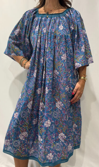 Robe Sita Bleu Mauve -Femme portant une robe ample en coton bleu et mauve à imprimé floral, manches larges et col smocké en dentelle