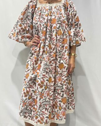 Robe Sita Blanche fleurie-Femme portant une robe ample en coton blanche à imprimé floral, manches larges et col smocké en dentelle