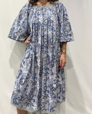 Robe Sita Bleu -Femme portant une robe ample en coton bleu gris à imprimé floral, manches larges et col smocké en dentelle