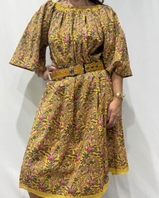 Robe Sita Jaune Fleurie -Femme portant une robe ample en coton jaune fleurie à imprimé floral, manches larges et col smocké en dentelle