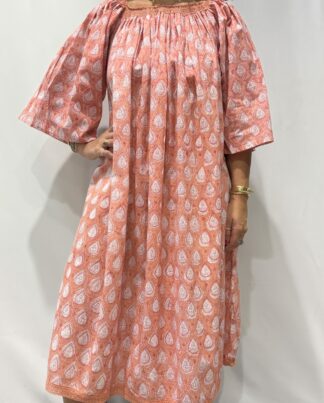 Robe Sita Saumon -Femme portant une robe ample en coton rose saumon à imprimé floral, manches larges et col smocké en dentelle