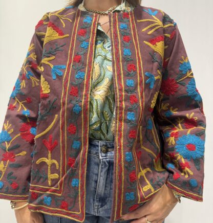 Veste Jaya de Micasasté pour femme, brodée, fond vieux rose et marron chaud, ornée de motifs floraux jaunes, rouges et bleu clair, coupe droite et manches longues.