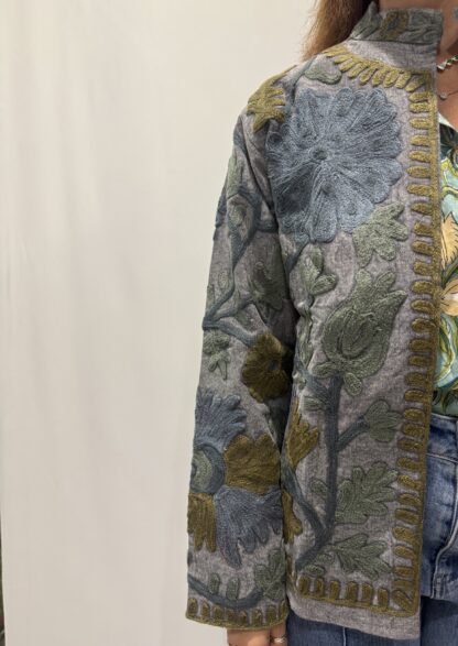 Veste Kamala de Micasasté pour femme, brodée de motifs verts, bleus et kaki sur fond bleu gris.