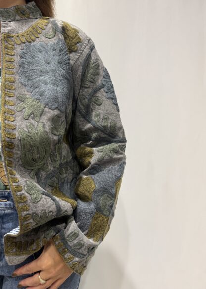 Veste Kamala de Micasasté pour femme, brodée de motifs verts, bleus et kaki sur fond bleu gris.
