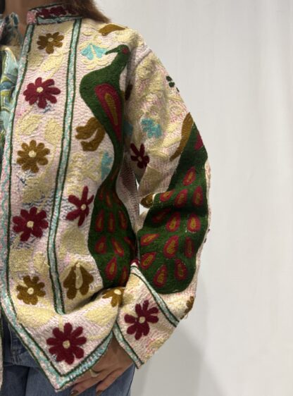Veste Kiara de Micasasté pour femme, brodée de fleurs bordeau et kaki clair et de paons vert foncé, bordeau et kaki sur fond rose pâle.