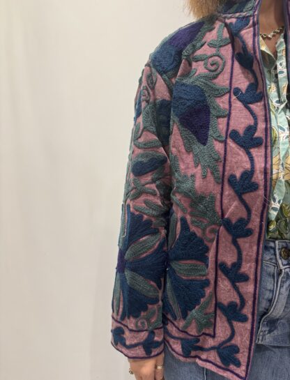 Veste Lalita de Micasasté pour femme, brodée, fond vieux rose, ornée de motifs végétaux bleu foncé, vert et violet, coupe droite et manches longues.