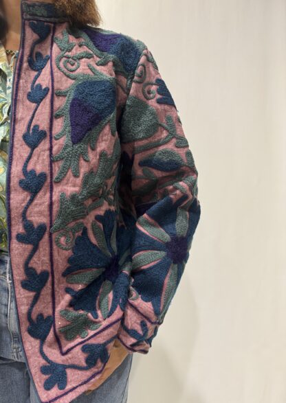 Veste Lalita de Micasasté pour femme, brodée, fond vieux rose, ornée de motifs végétaux bleu foncé, vert et violet, coupe droite et manches longues.