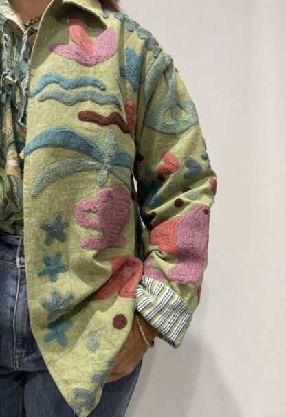 Veste Veda de Micasasté portée de profil gauche, motifs floraux détaillés sur fond vert.Une veste courte suzani embrodery aux manches longues et col mao.