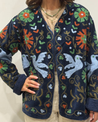 Femme portant la veste Eshna en velours bleu marine brodé à la main, avec motifs colorés et doublure bleu marine.