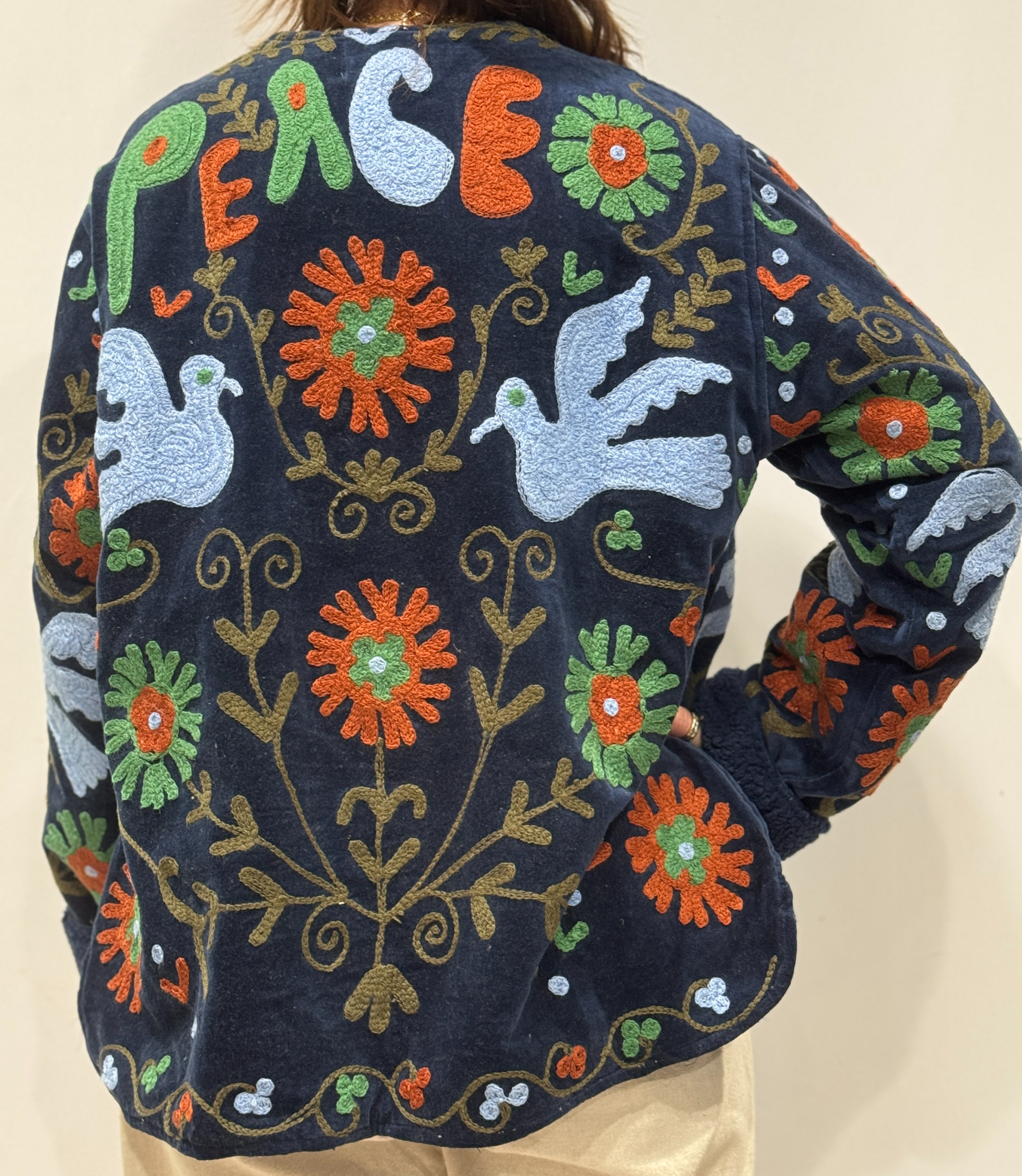 Détail du dos de la veste Eshna, avec oiseaux brodés, fleurs colorées et mot “PEACE” brodé en haut.