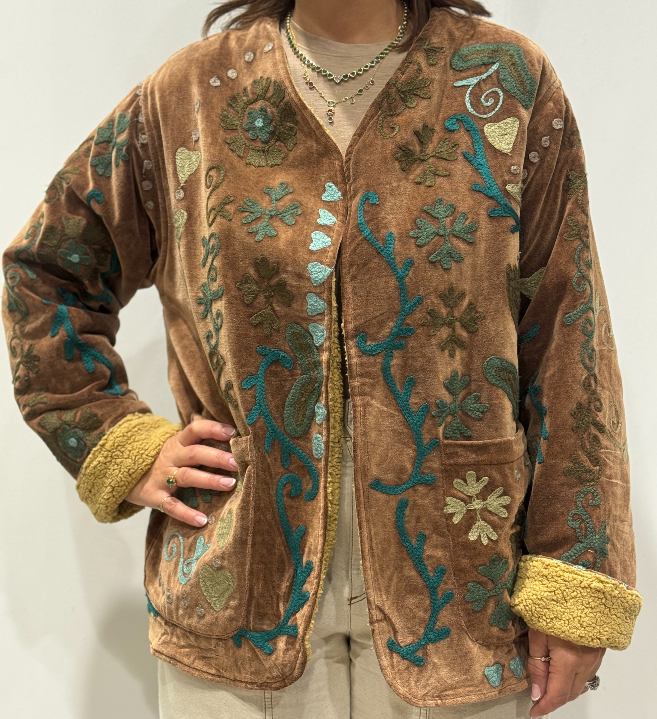 Femme portant la veste Kaira en velours marron brodé à la main, avec doublure beige et motifs floraux.