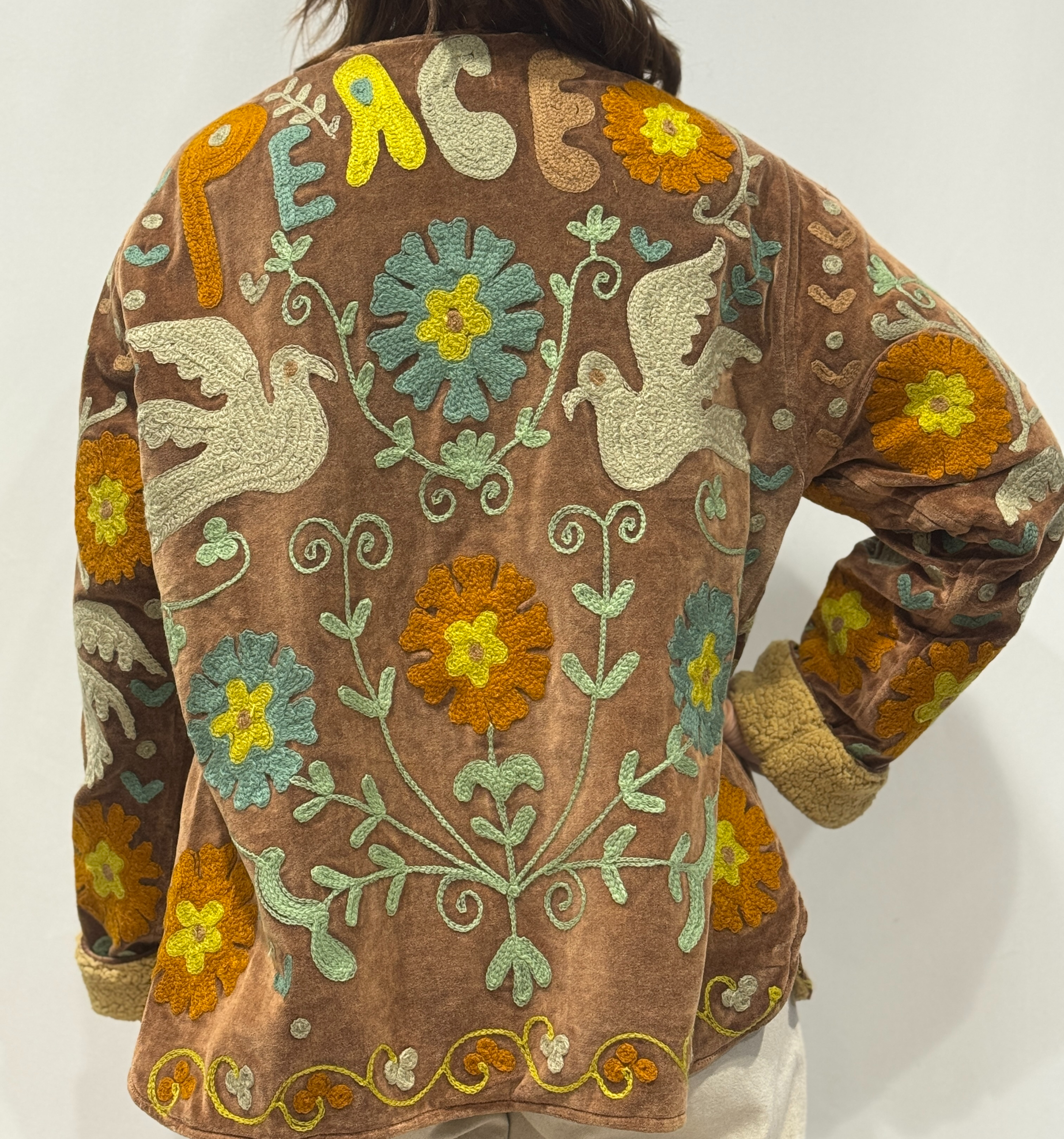 Détail du dos de la veste Luna, avec motifs floraux colorés et le mot “PEACE” brodé en haut.