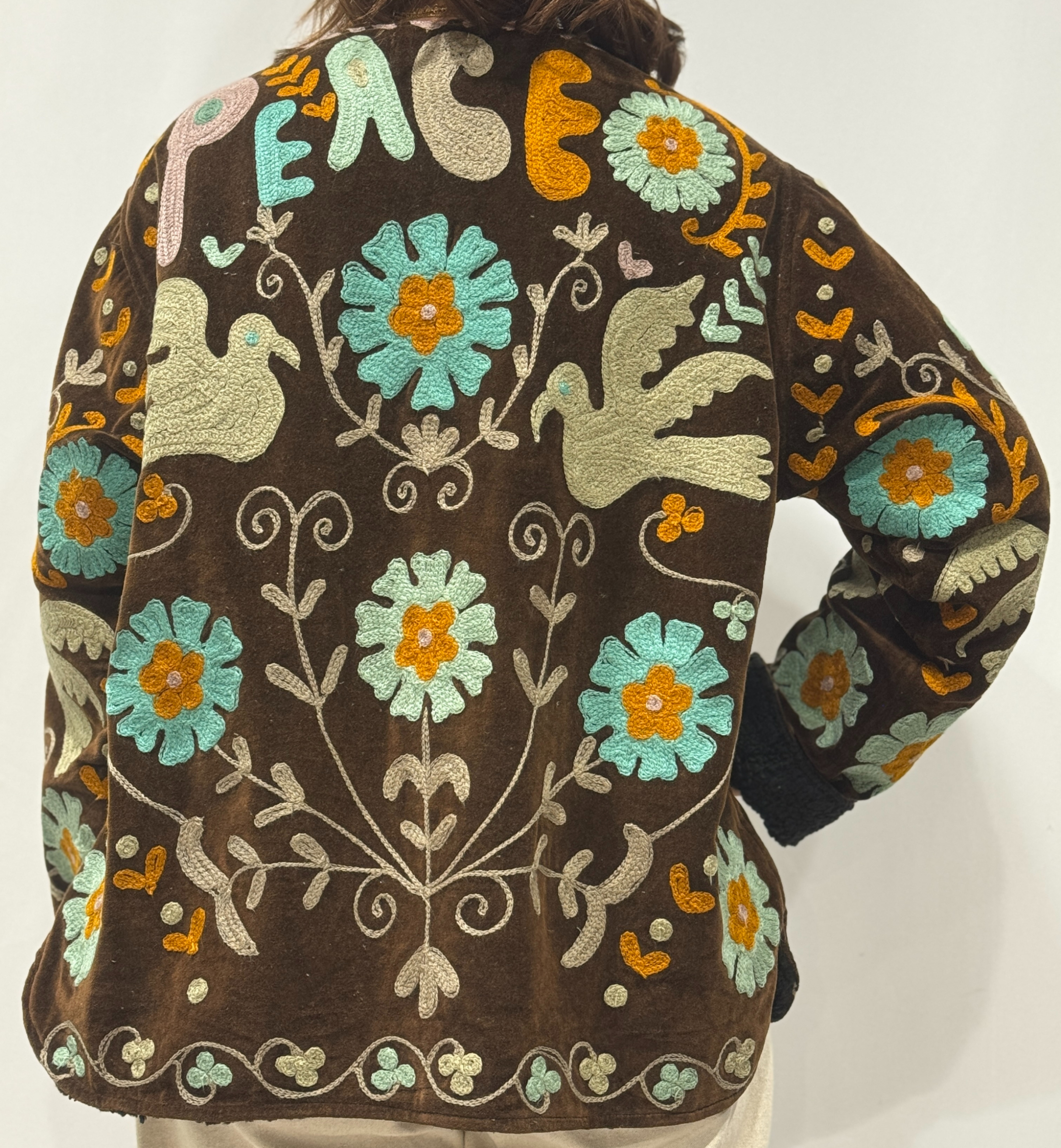 Détail du dos de la veste Miraï, avec motifs floraux colorés et le mot “PEACE” brodé en haut.