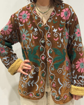 Femme portant la veste Nalina en velours marron brodé à la main, avec doublure beige et motifs colorés.