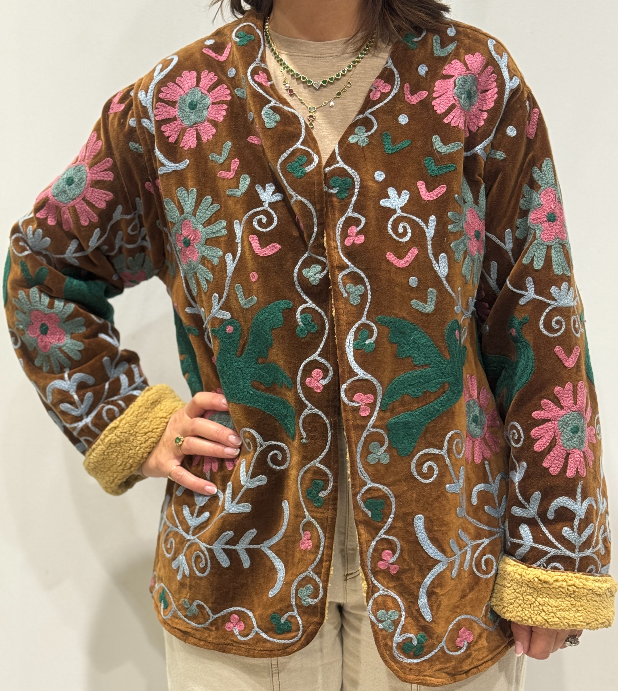 Femme portant la veste Nalina en velours marron brodé à la main, avec doublure beige et motifs colorés.