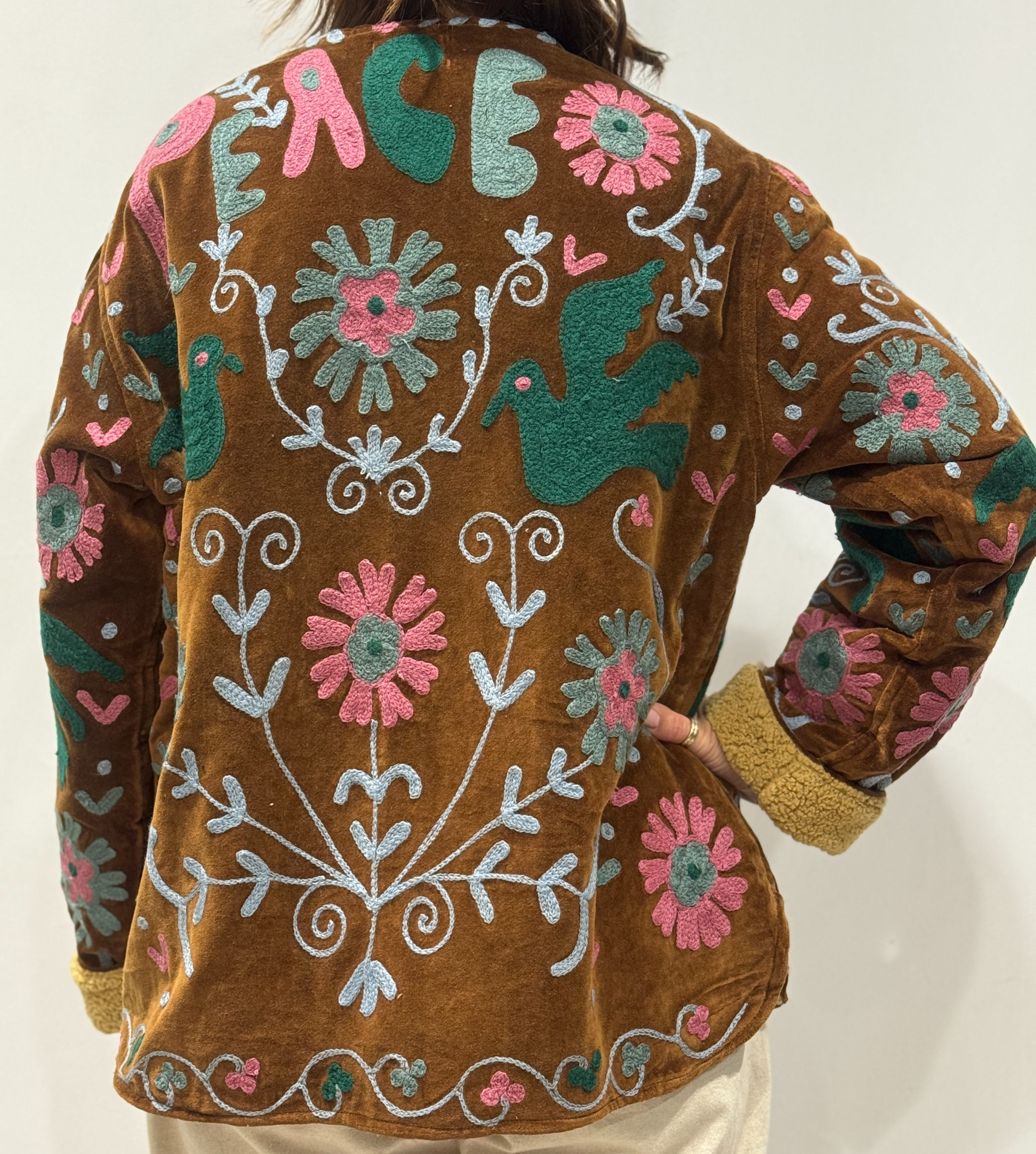 Détail du dos de la veste Nalina, avec oiseaux brodés, fleurs colorées et mot “PEACE” brodé en haut.