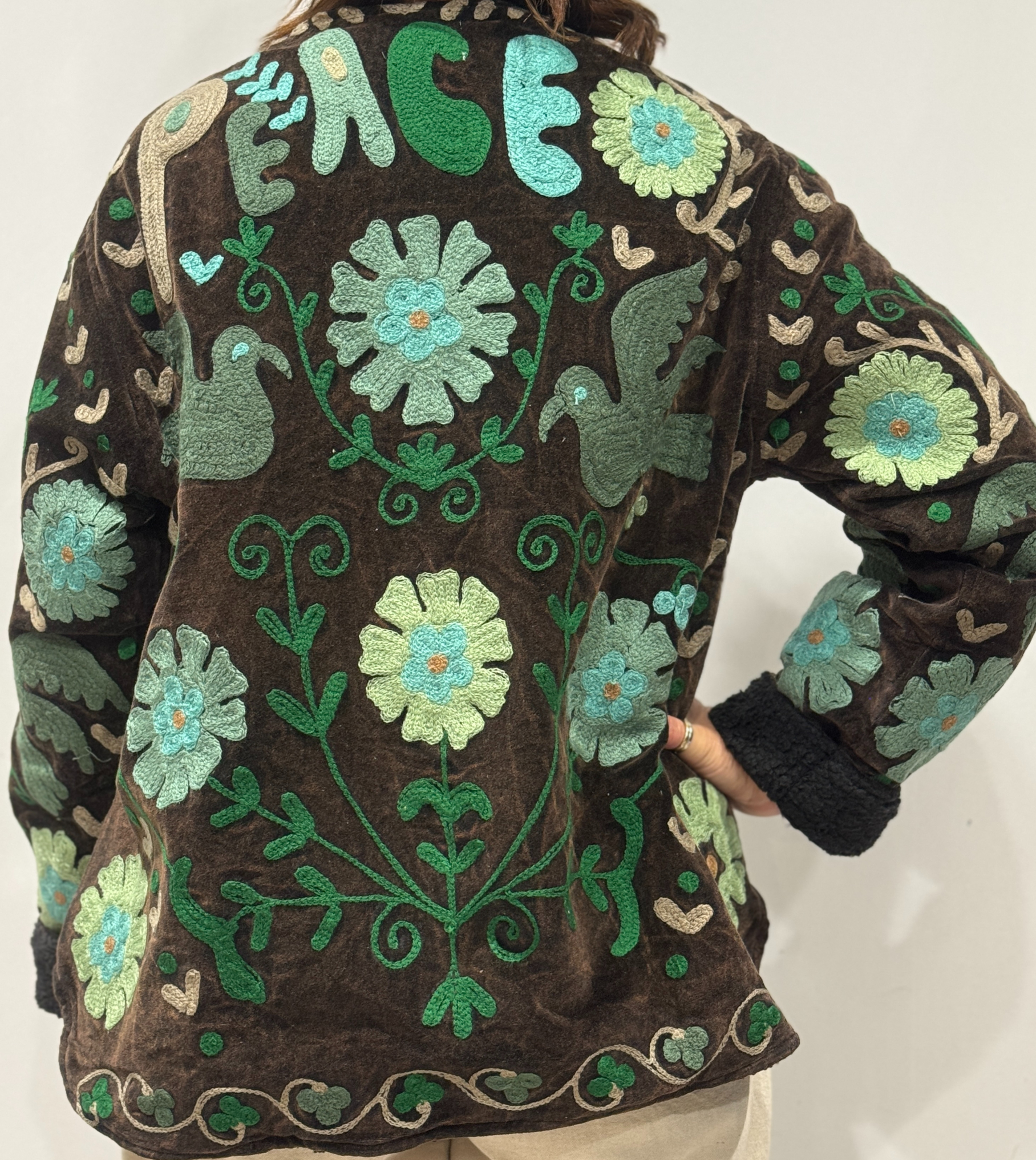 Détail du dos de la veste Sahra, avec oiseaux brodés, fleurs colorées et le mot “PEACE” brodé en haut.